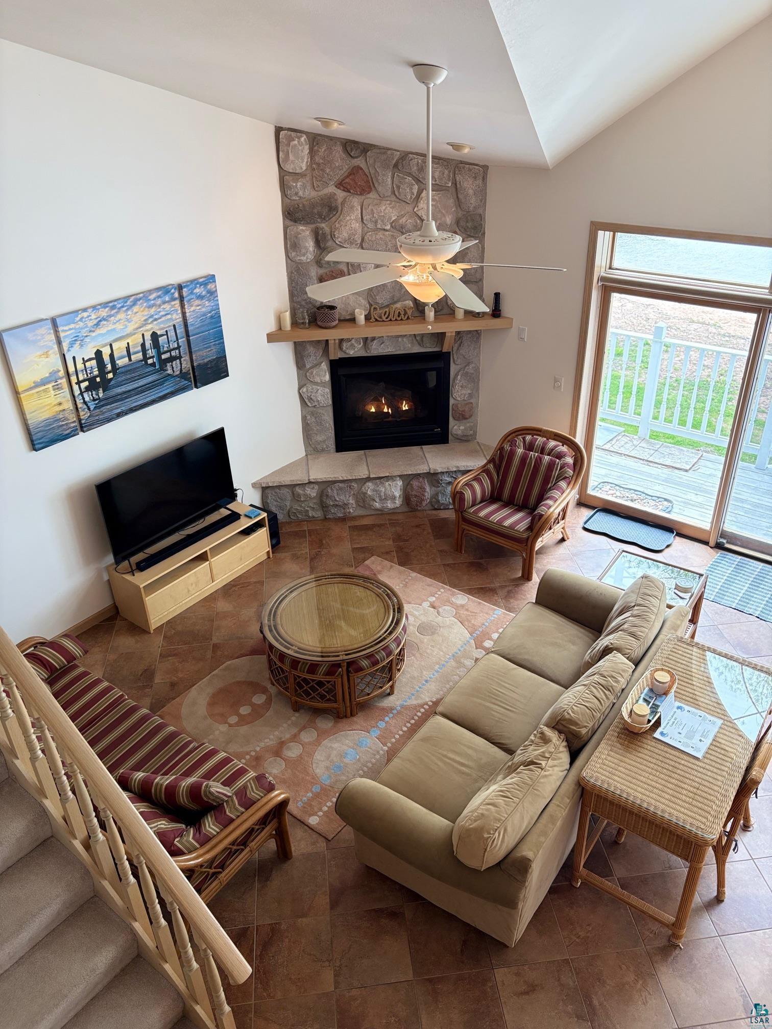 Image 3: Tiled living area featuring ceiling fan, a stone fireplace, and lofted ceiling, Living Room