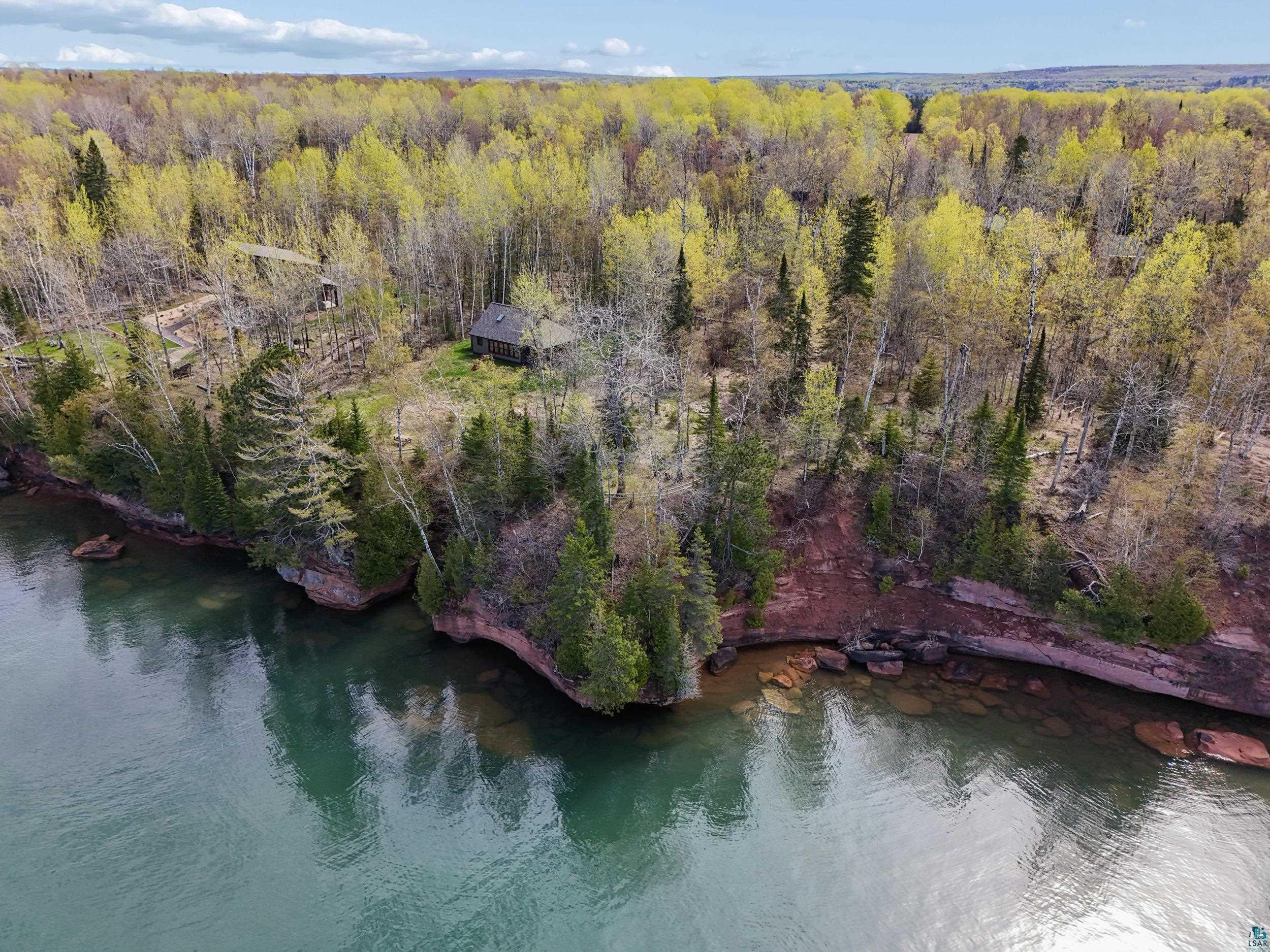 Image 0: Wooded waterfront property featuring a rustic cabin set against a backdrop of mature trees, Aerial View