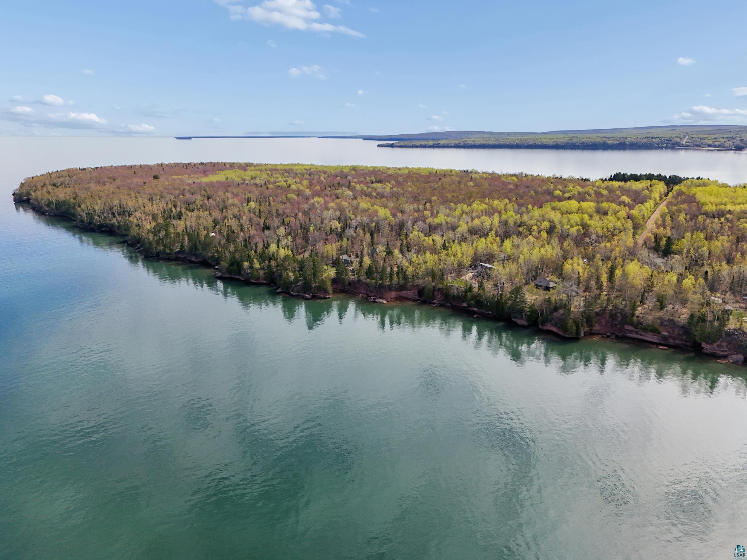 Image 3: Expansive waterfront property featuring mature deciduous and evergreen trees, a rocky shoreline, and two distinct structures, View