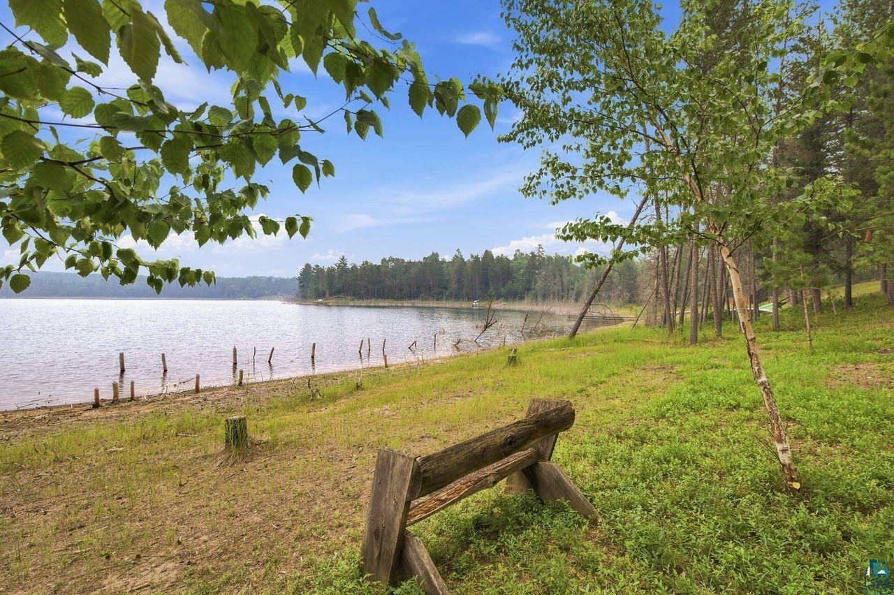 Image 1: Shoreline property featuring a tranquil lake, natural wooded surroundings, and a rustic wooden bench, View
