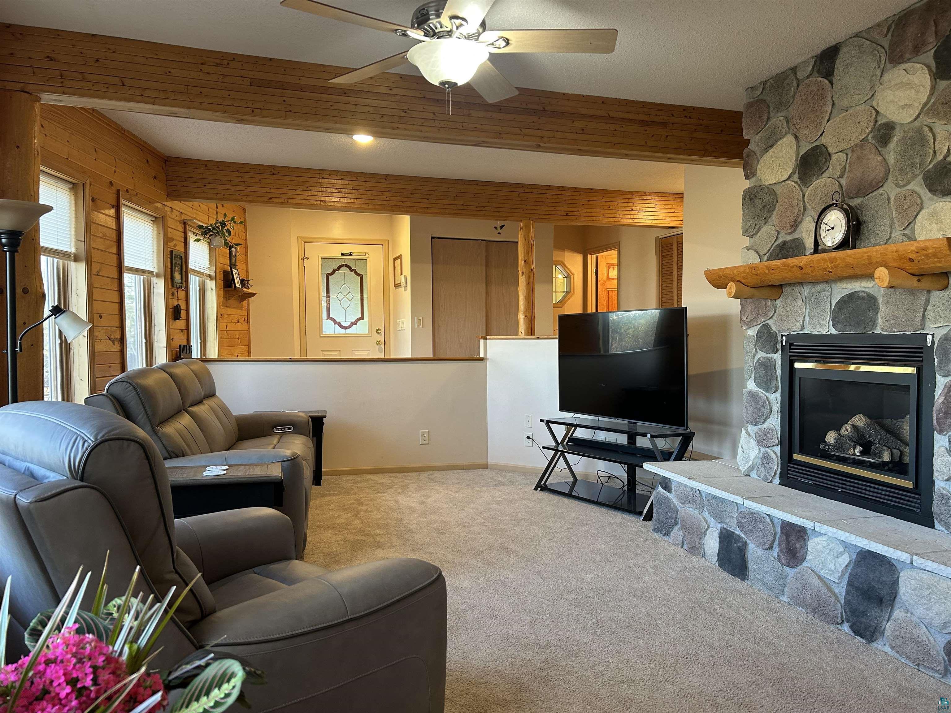 Image 1: Carpeted living room featuring ceiling fan, a fireplace, wooden walls, and beam ceiling, Living Room