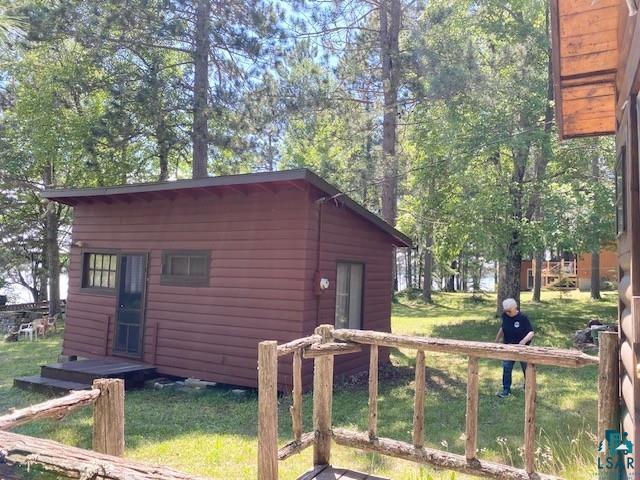 Image 0: Brown horizontal siding building with a dark screen door, set on a grassy lot with mature trees, Out Buildings
