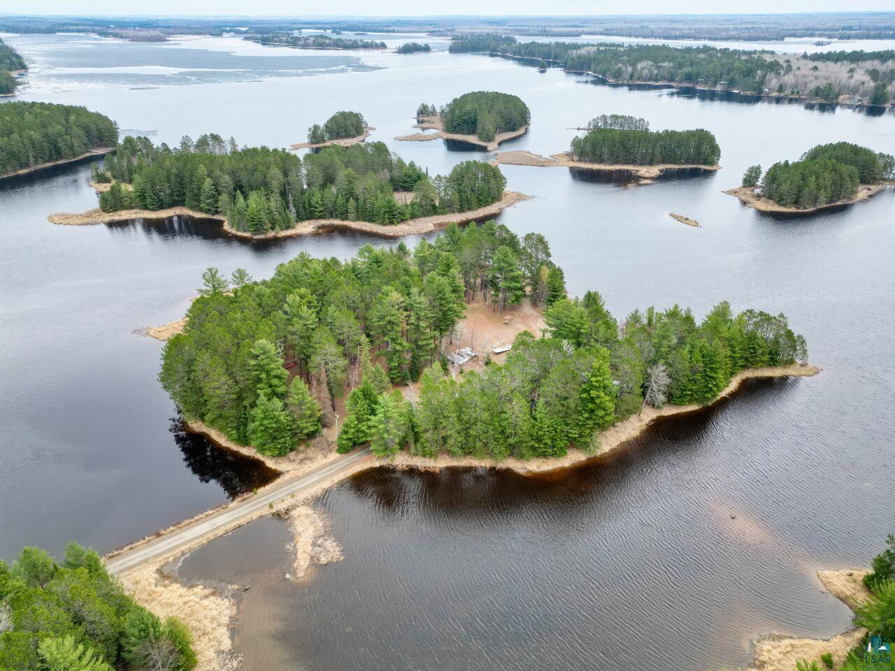 Image 1: Island property featuring mature evergreen trees, a private gravel road, and water frontage, Aerial View
