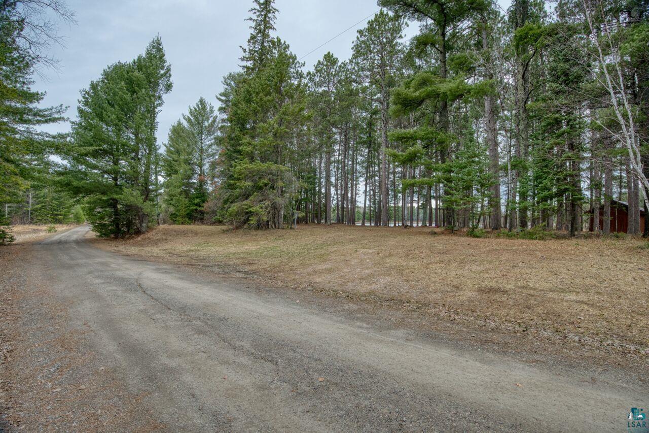 Image 3: Gravel driveway leading to a treed parcel with a rustic outbuilding, Community