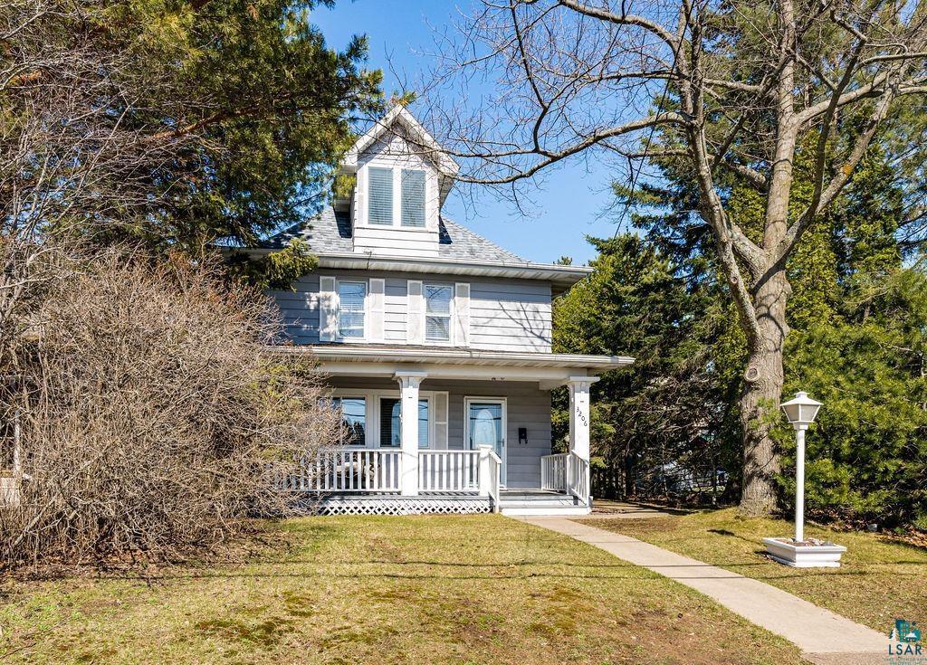 Image 3: Charming three-story residence featuring a covered front porch with white railings, a dormer window, and a light-colored exterior with shutters, Front of Home