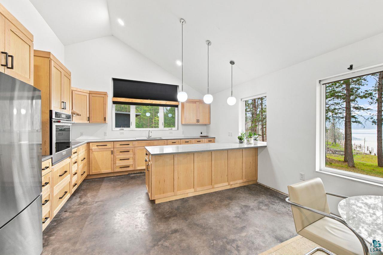 Image 3: Kitchen featuring vaulted ceilings, light wood cabinetry with dark hardware, stainless steel appliances, a center island with pendant lighting, and multiple windows, Kitchen
