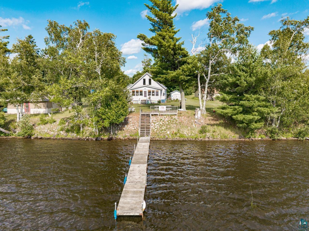 Image 0: Waterfront property featuring a private dock extending into the water, a white siding home, and mature trees on a sloped lot, Dock