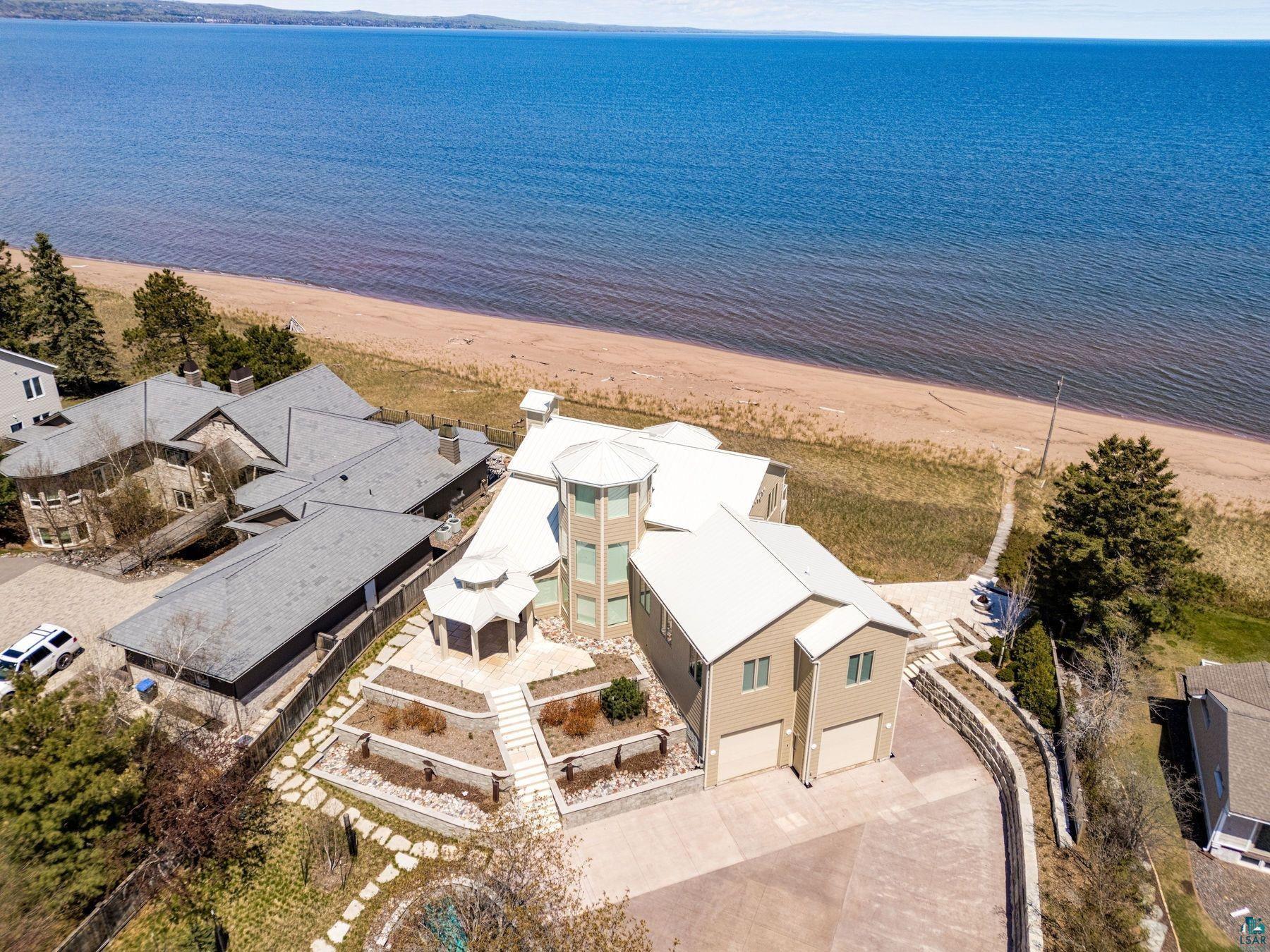 Image 1: Expansive waterfront property featuring direct beach access, a multi-level main residence, tiered landscaping with a gazebo, and an attached two-car garage, Aerial View