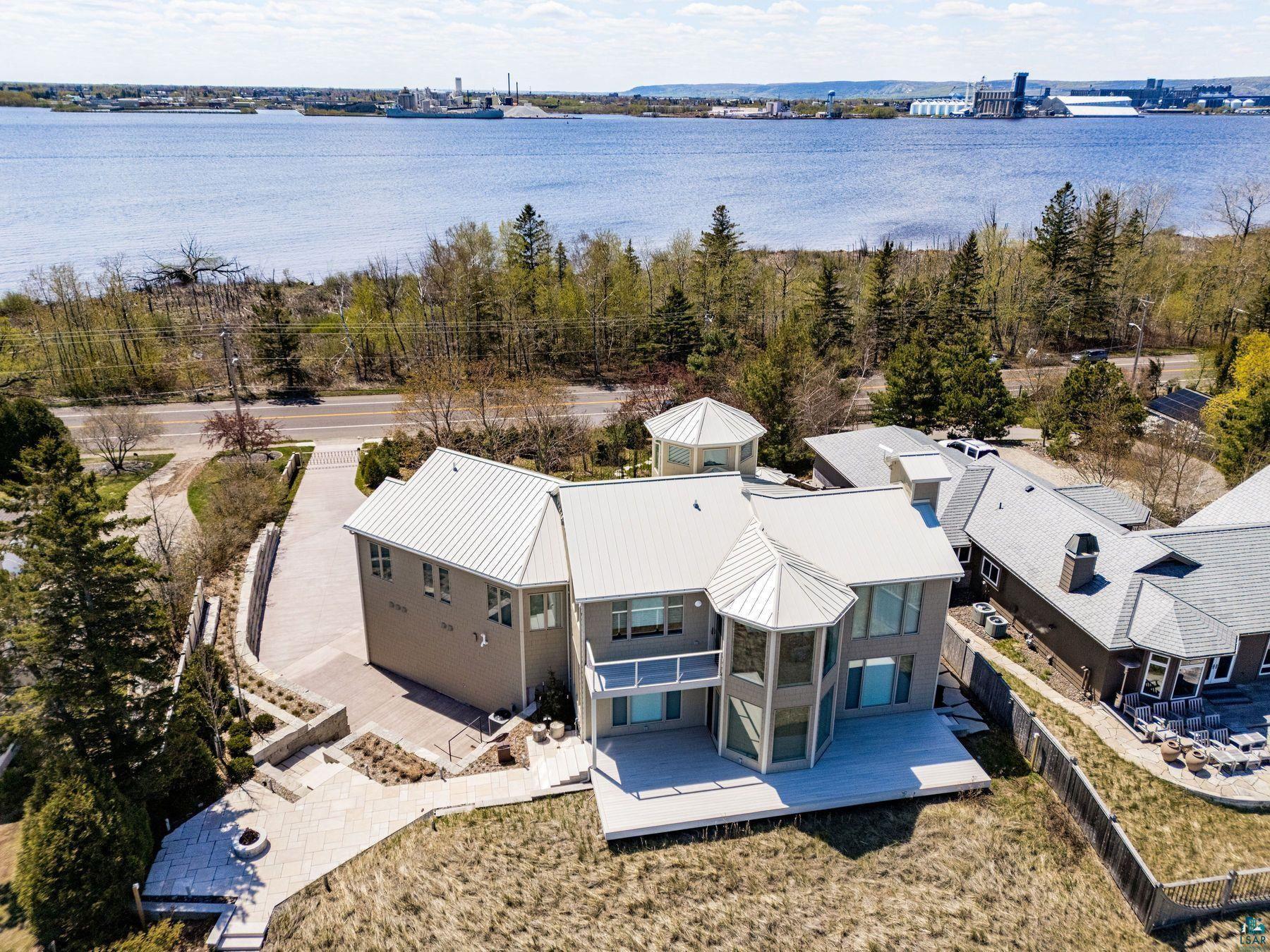 Image 2: Contemporary residence featuring multiple levels, a prominent water backdrop, extensive decking, a circular turret, and a metal roof, Aerial View
