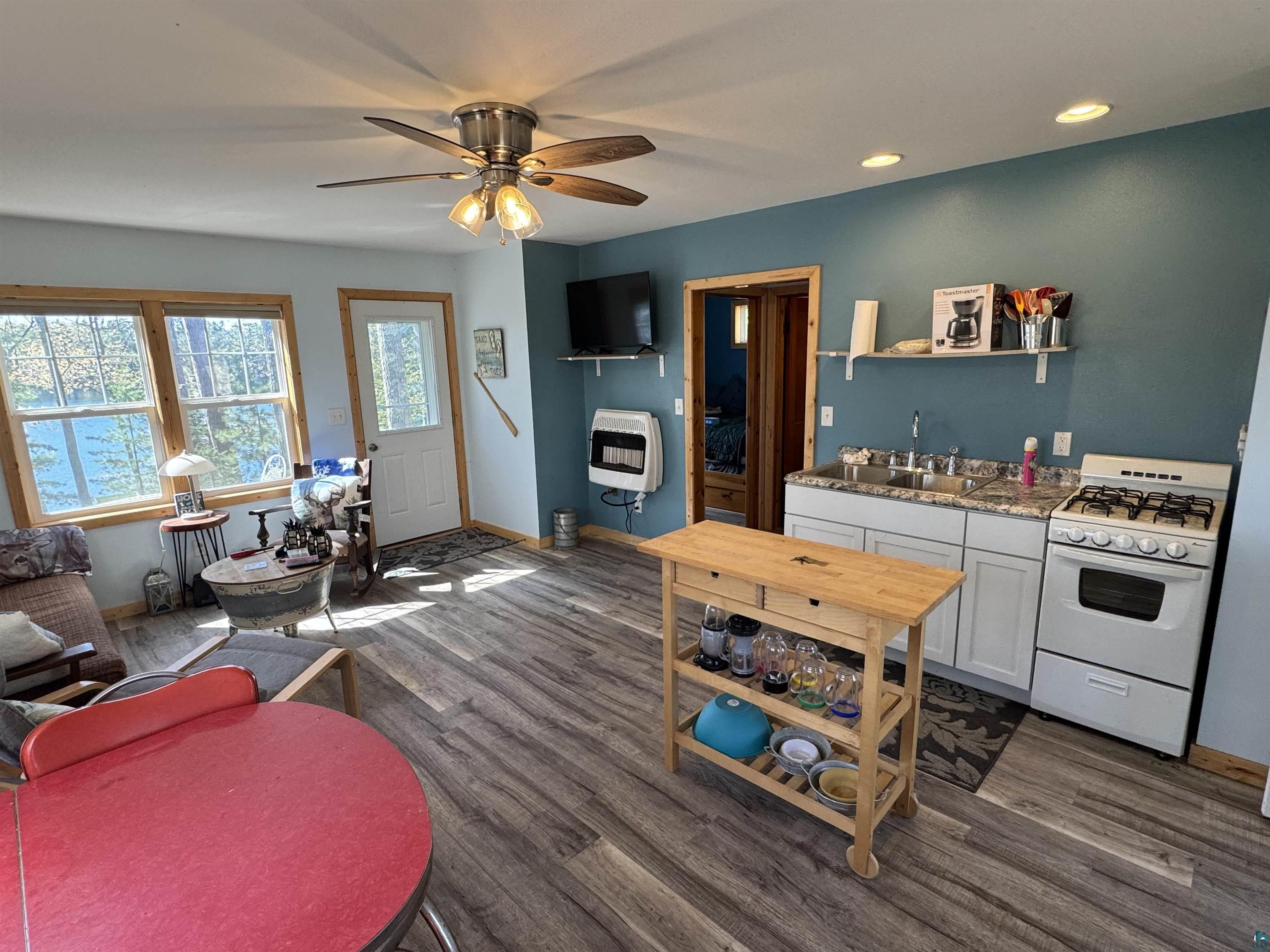 Image 1: Open-concept living area featuring wood-finish flooring, a ceiling fan with integrated lighting, recessed lighting, and a white kitchen with a built-in sink and stove, Kitchen