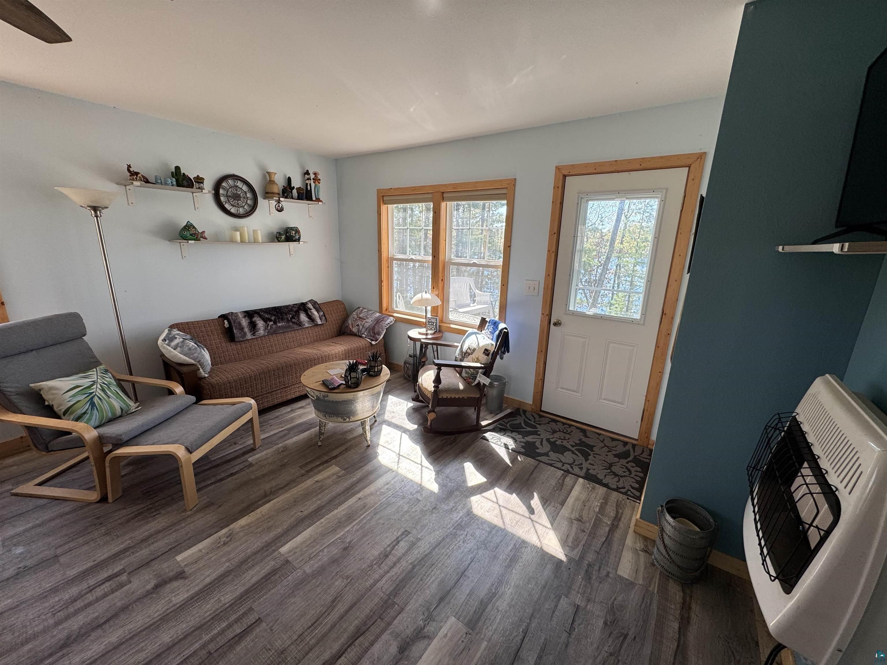 Image 3: Living space featuring wood-finish flooring, light blue walls, natural wood trim, and a white entry door with a window, Living Room