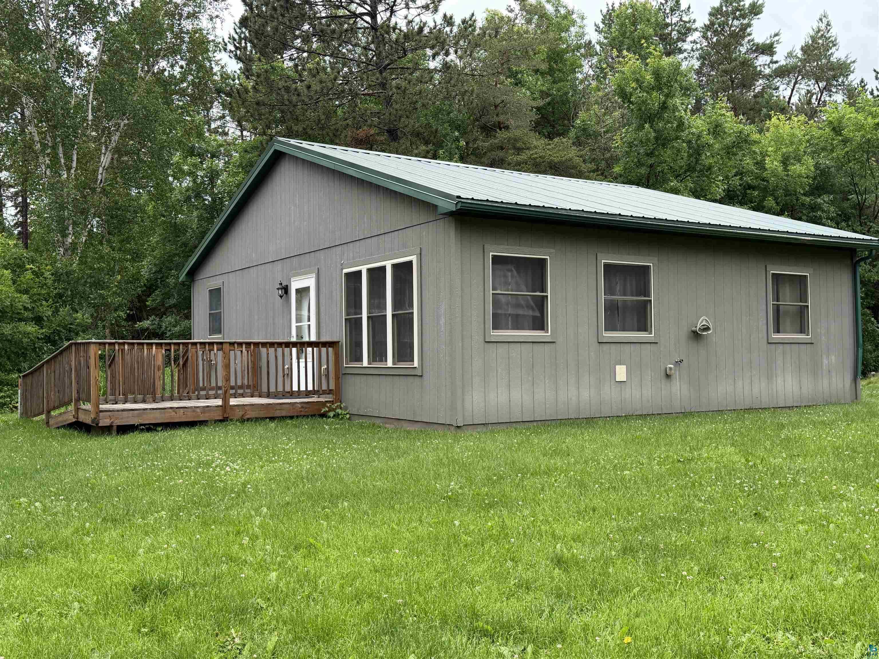 Image 0: Gray-sided structure featuring a green metal roof and a wooden deck with railing, One level living