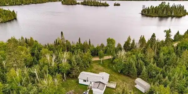 Image 1: Lakeside property featuring a single-story residence with a gray shingle roof and a wooden deck, Aerial View