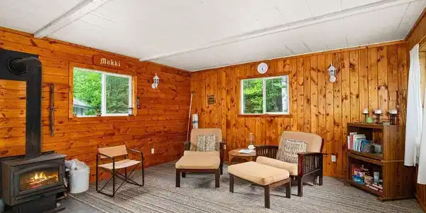 Image 2: Room featuring natural wood paneling, a wood-burning stove with a visible flame, and a white planked ceiling, Sitting Room