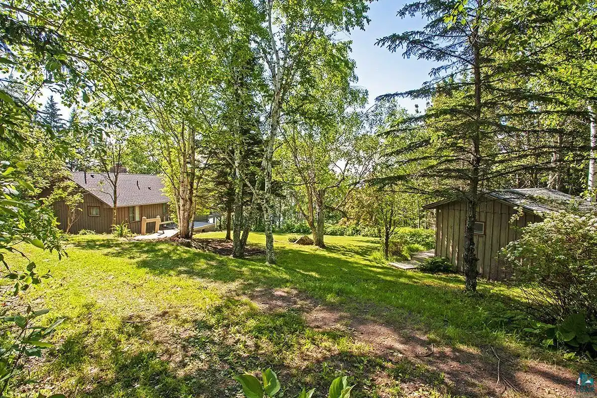 Image 0: Expansive green space featuring mature trees and a rustic shed with a shingle roof, Yard