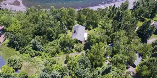 Image 3: Property situated amidst dense mature trees, featuring a gray pitched roof structure and a waterside location, Aerial View