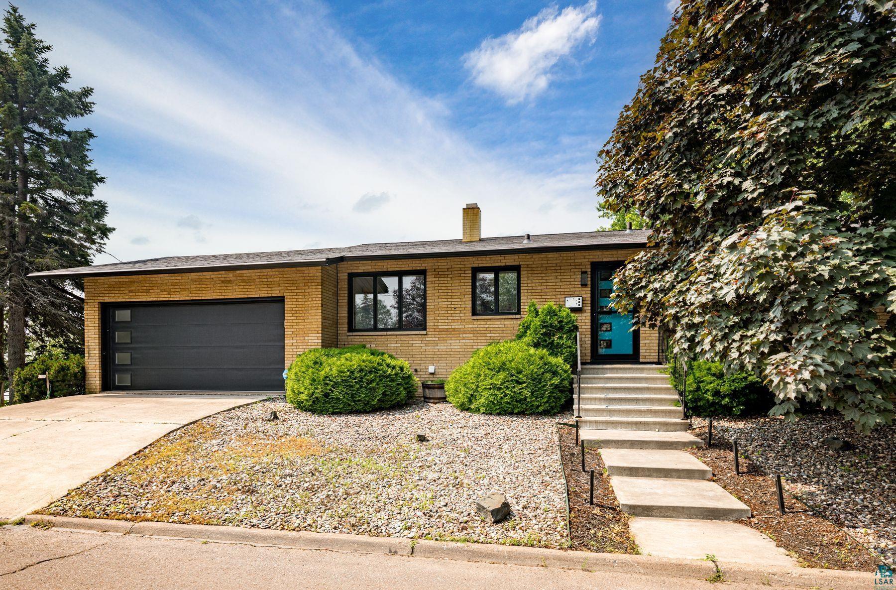 Image 0: Mid-century modern residence featuring a light brick exterior, a contemporary dark gray garage door with square window inserts, and black-framed windows, Front Of Structure
