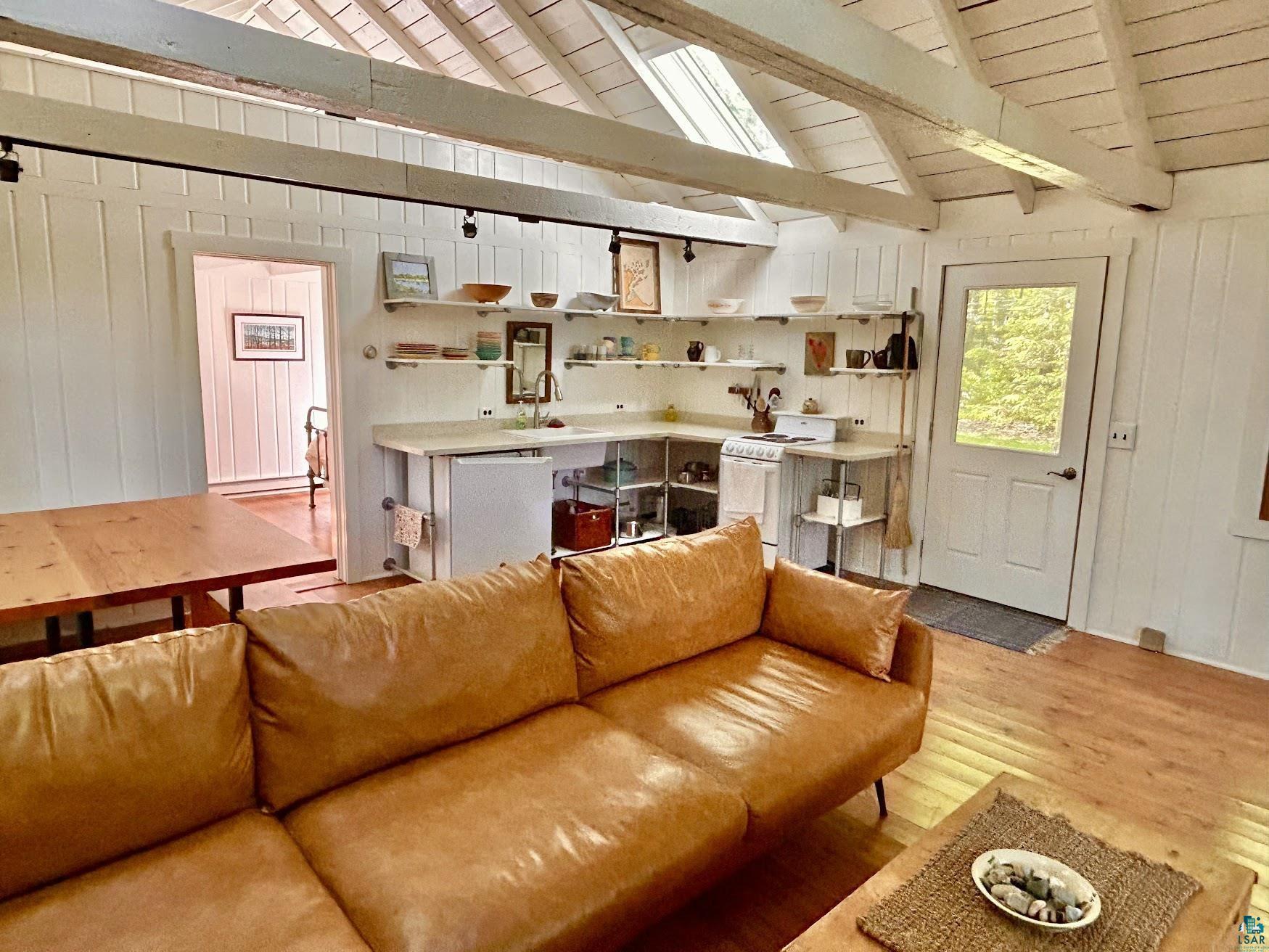 Image 1: Vaulted wood-finish ceiling with exposed beams, wood-finish flooring, white panel walls, open shelving, and a glass-paneled exterior door, Living Room