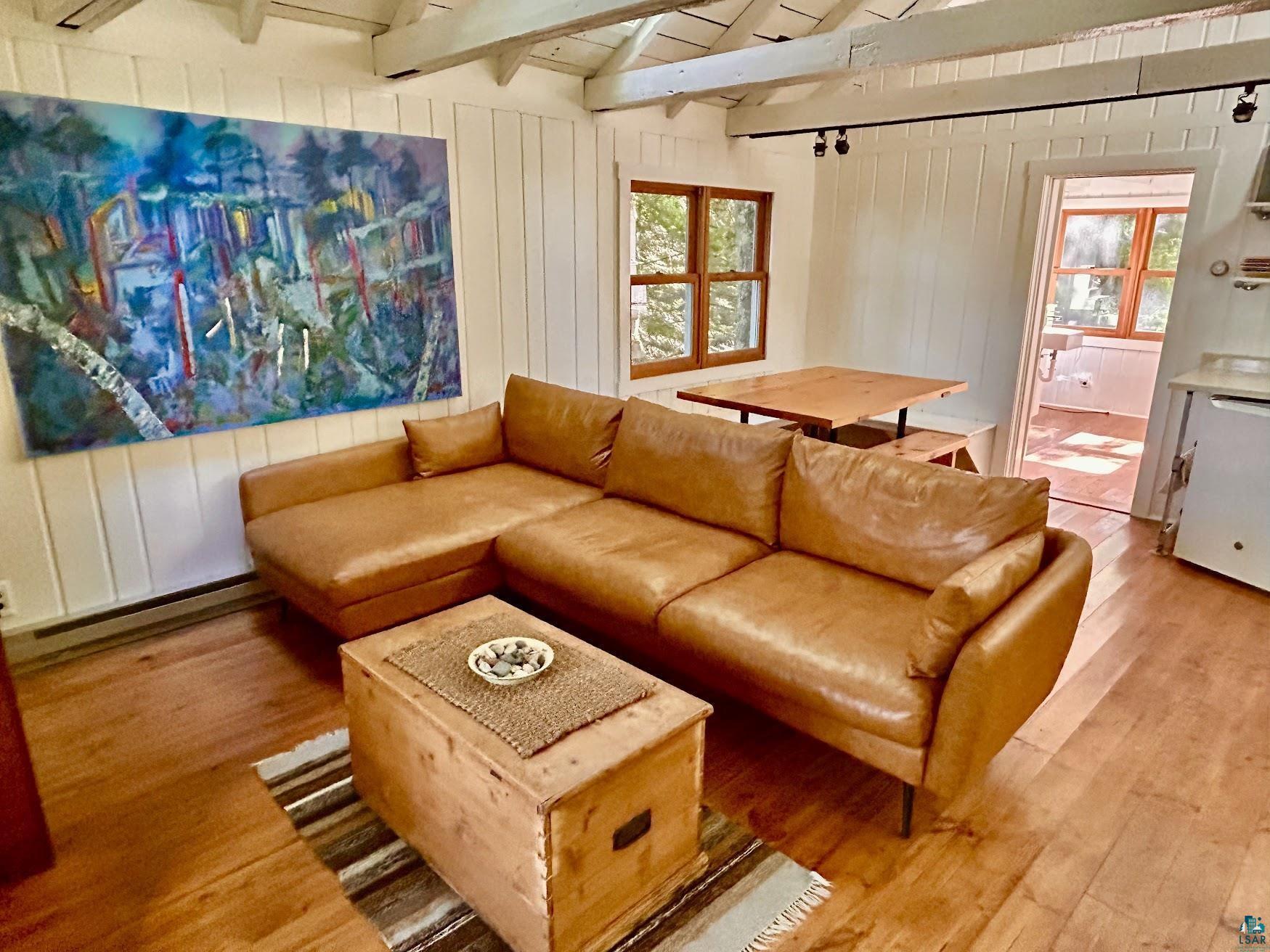 Image 2: Bright interior space featuring vaulted ceilings with exposed beams, wood-finish flooring, and white paneled walls, Living Room
