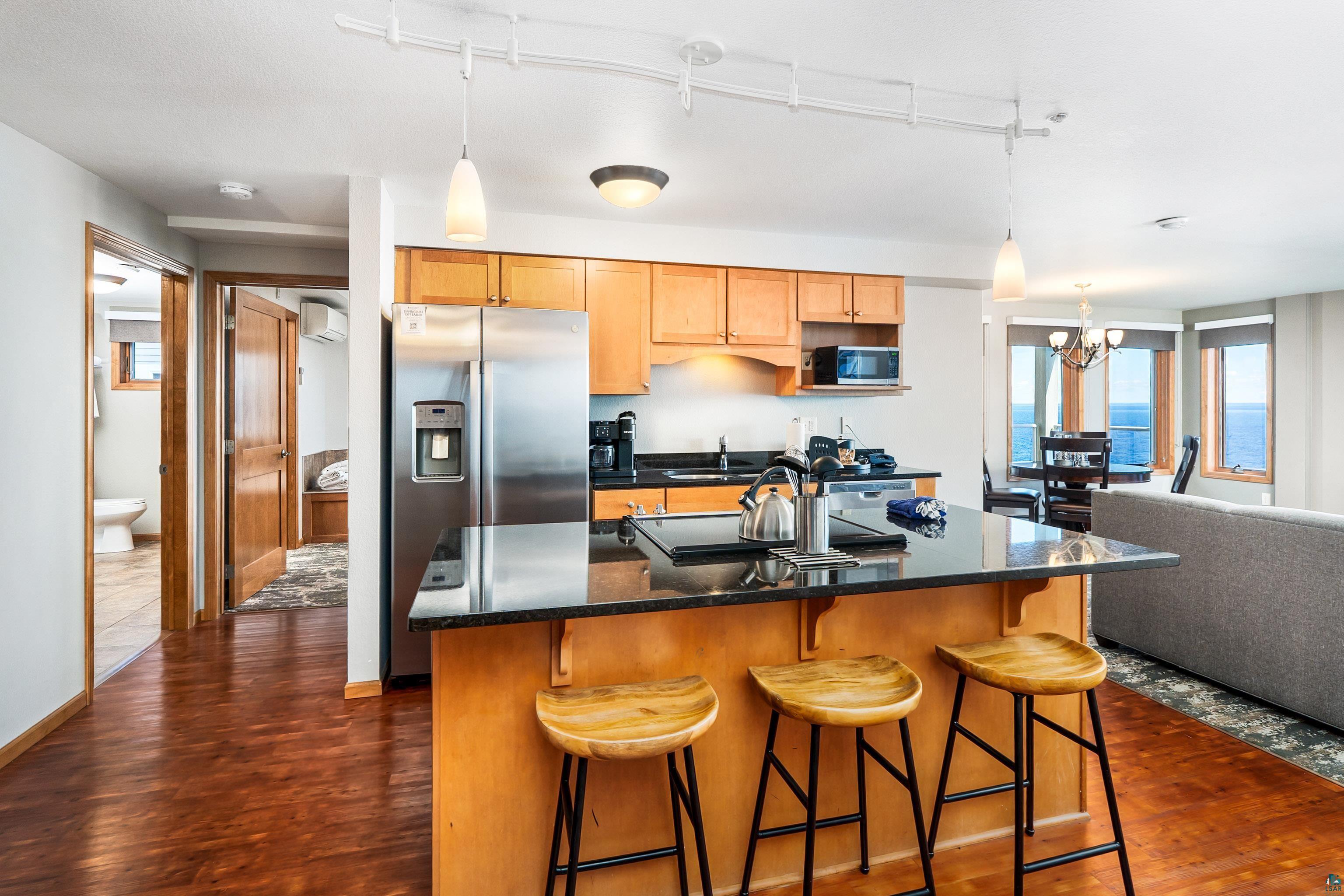 Image 5: Open-concept kitchen featuring wood-finish flooring, stainless steel appliances, and a central island with a dark countertop and breakfast bar seating, Kitchen