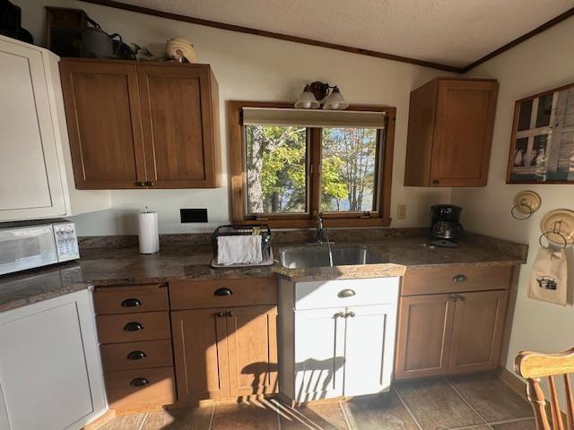 Image 3: Kitchen with a textured ceiling, crown molding, dark stone counters, white microwave, and brown cabinetry, Kitchen