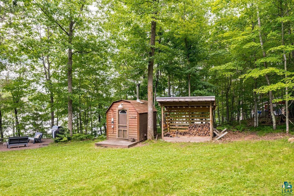 Image 1: Lush green lawn with a wood-sided outbuilding featuring a small deck and a metal chimney, Yard