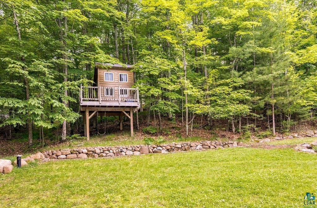 Image 3: Wood-sided elevated structure featuring a front balcony with wood railing, set within a lush tree-filled landscape, Yard