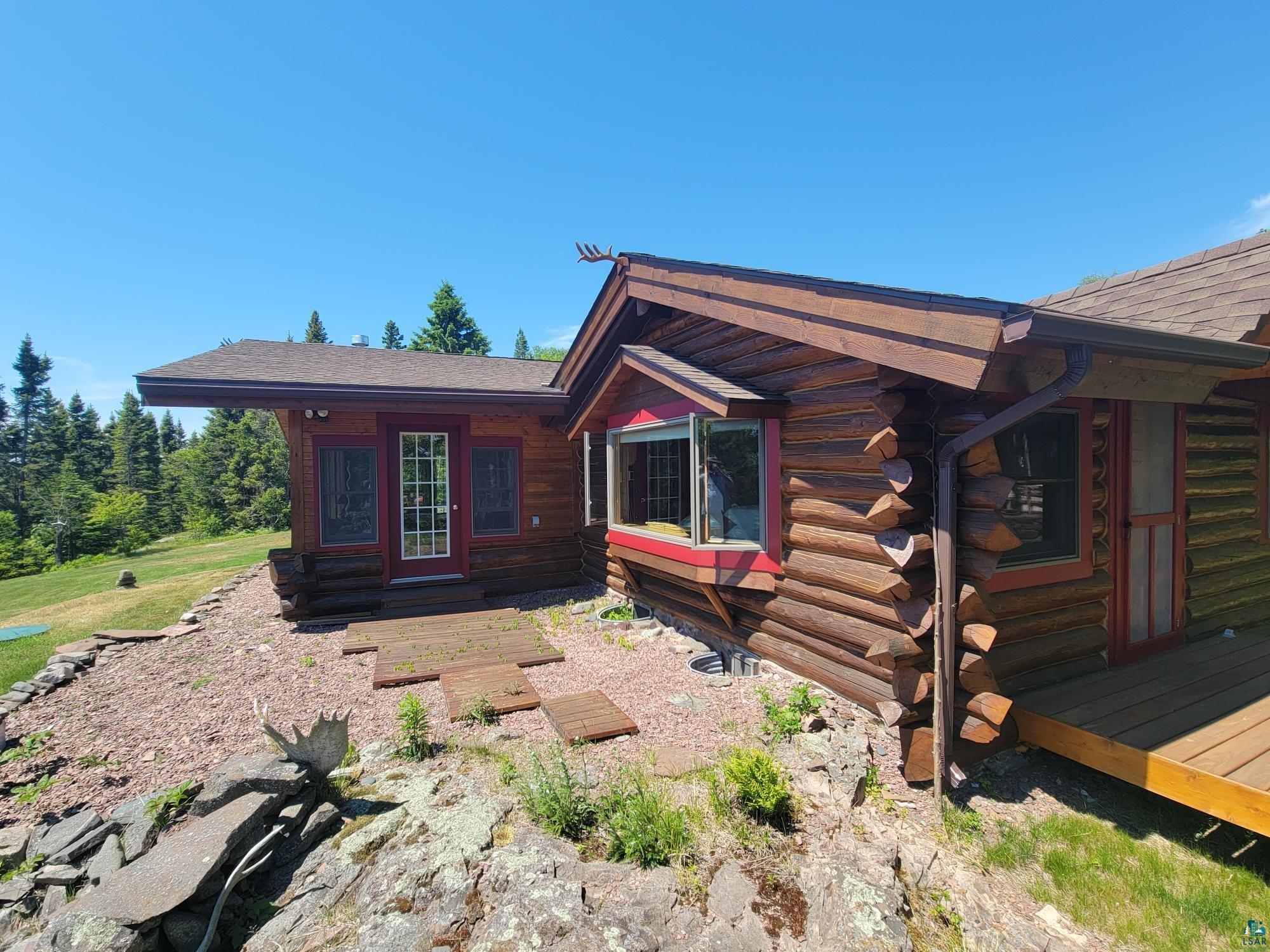Image 1: Rustic log home exterior featuring a prominent bay window with red trim, Side Of Structure