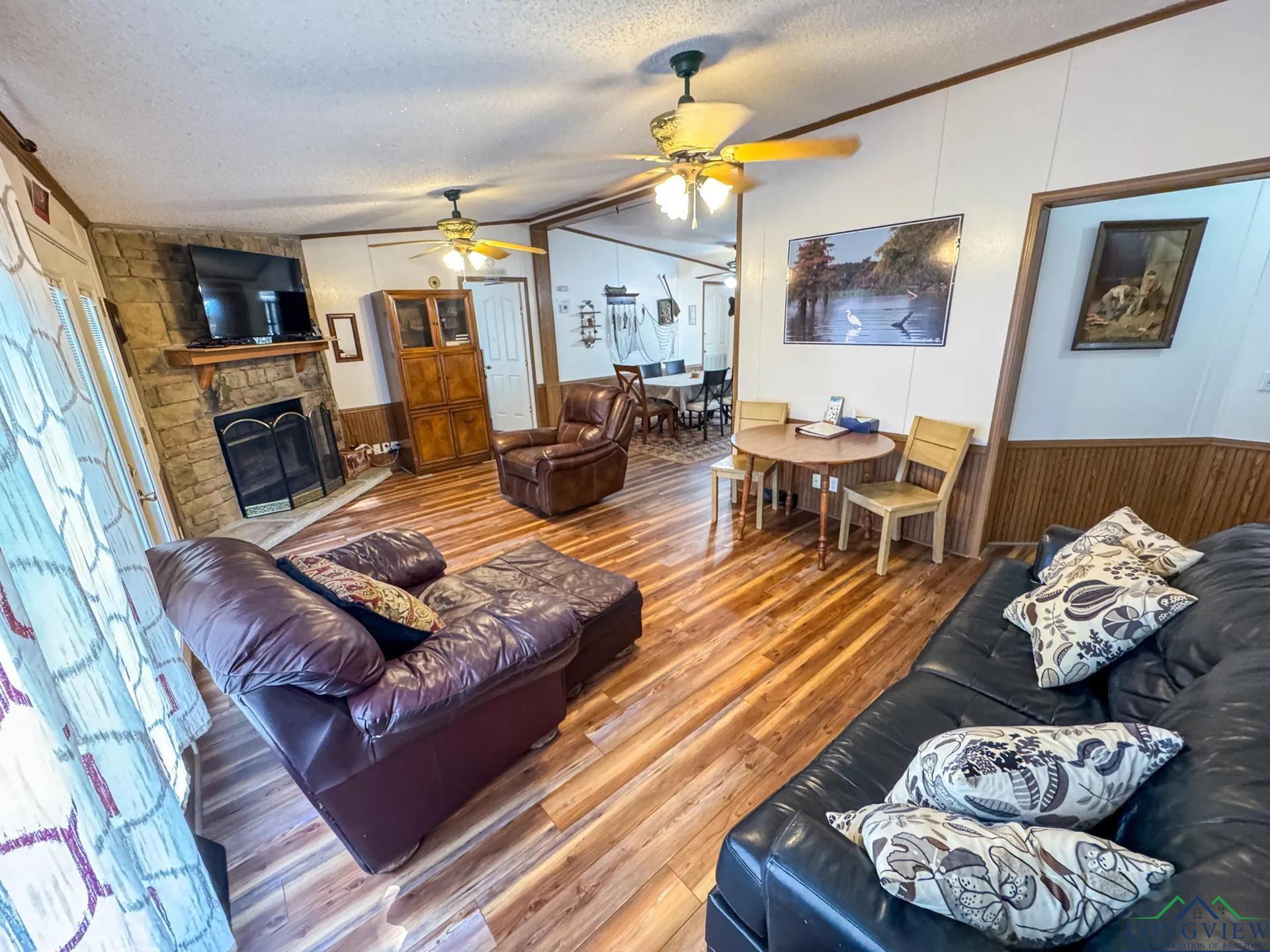 Image 3: Living room featuring a textured ceiling, wainscoting, wooden walls, a stone fireplace, and wood finished floors, Living Room