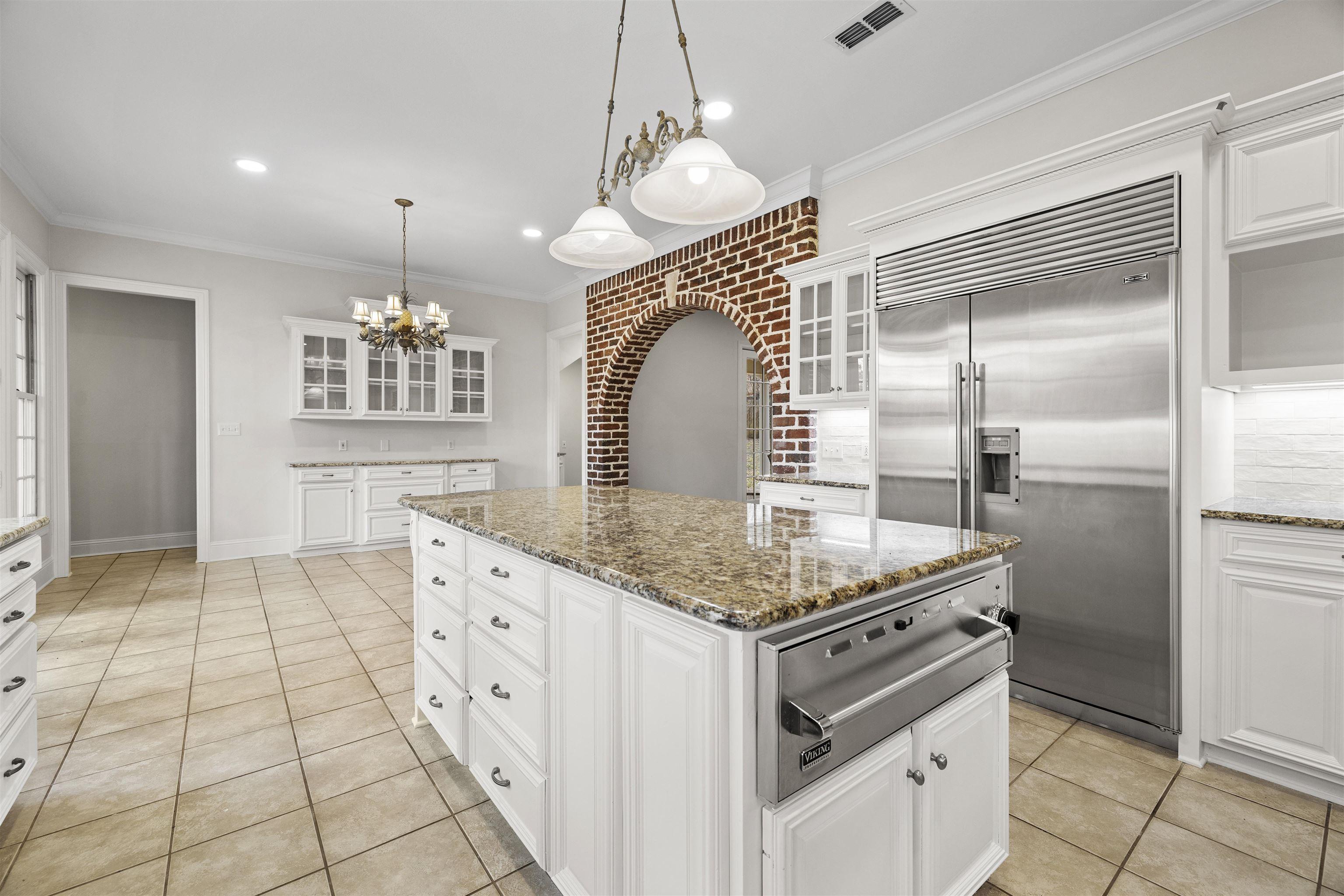 Image 4: Kitchen with glass insert cabinets, white cabinetry, built in fridge, light stone countertops, and crown molding, Kitchen