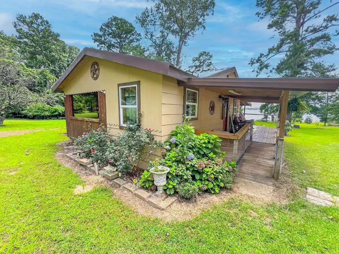 Image 0: Exterior featuring a covered wooden deck, a wooden ramp, and garden beds with mature shrubs, Side Of Structure
