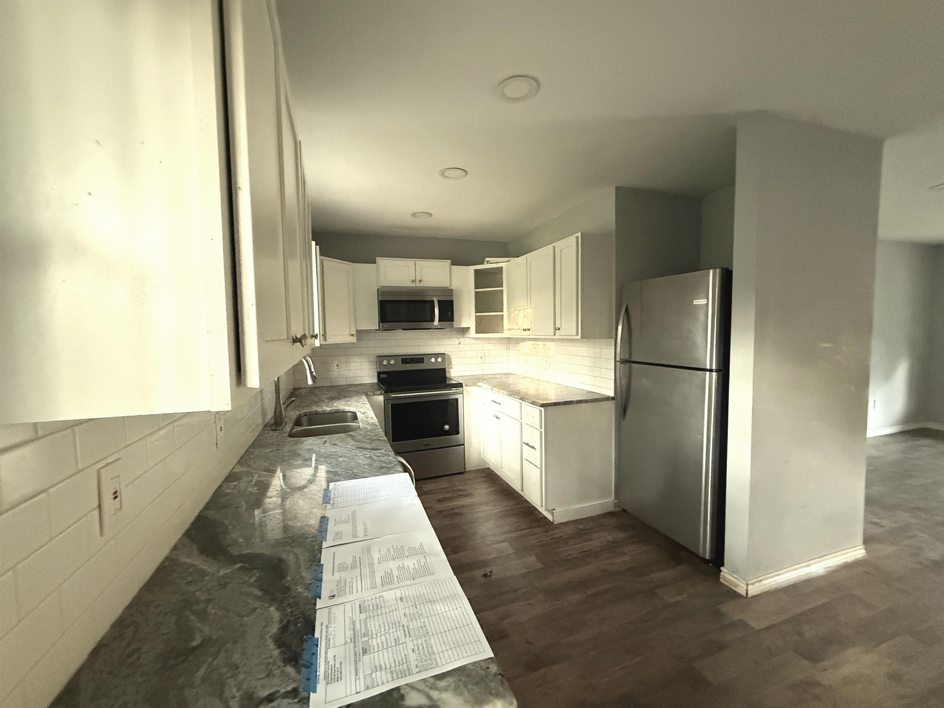 Image 2: Kitchen featuring white cabinetry, decorative backsplash, stainless steel appliances, light stone countertops, and dark wood finished floors, Kitchen