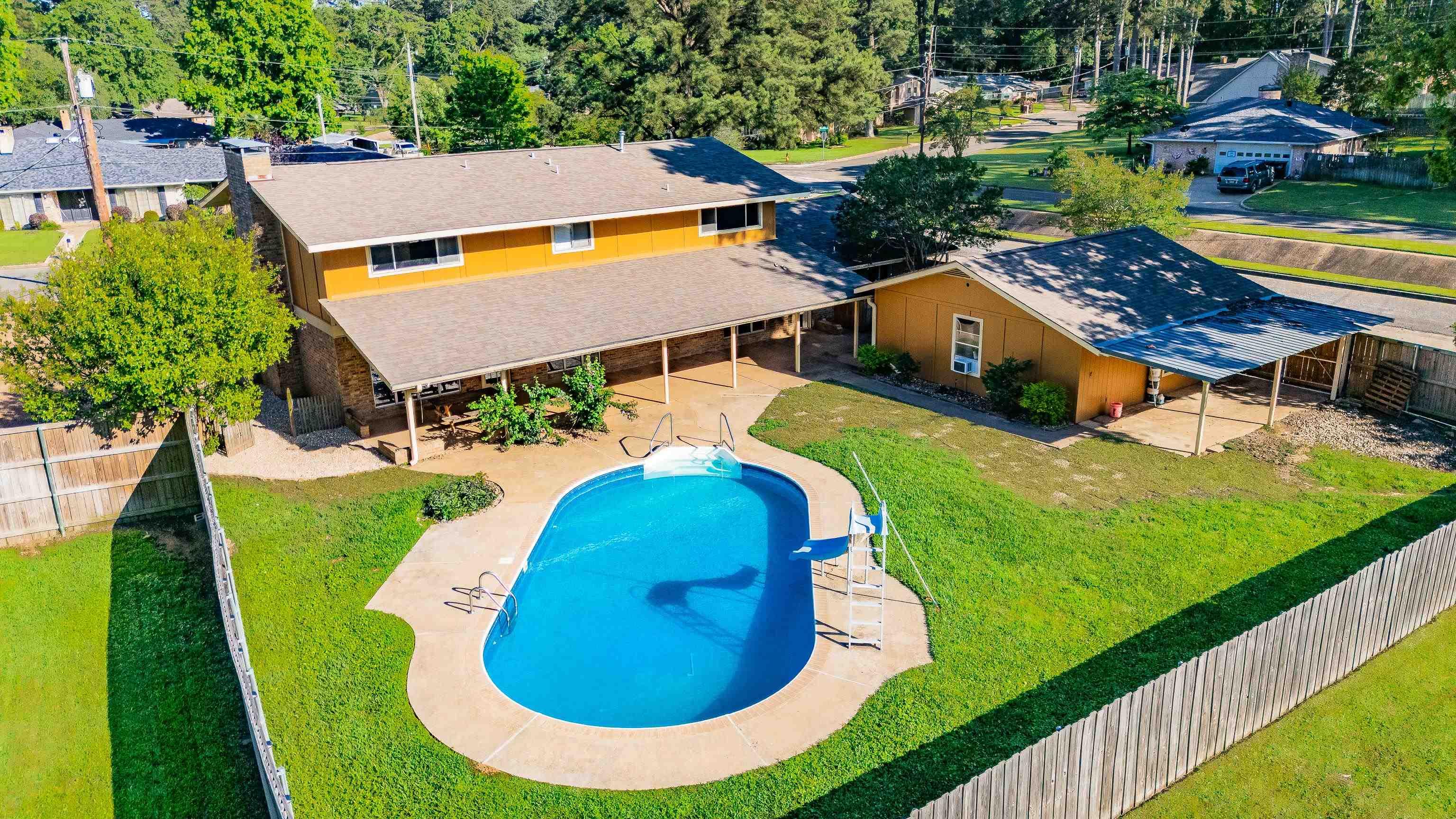 Image 2: Expansive backyard featuring a kidney-shaped swimming pool with concrete surround, a covered patio area, and a wood privacy fence, Pool