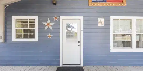 Image 1: Blue horizontal siding exterior with a white entry door, two multi-pane windows, and a wood-finish porch, Entry