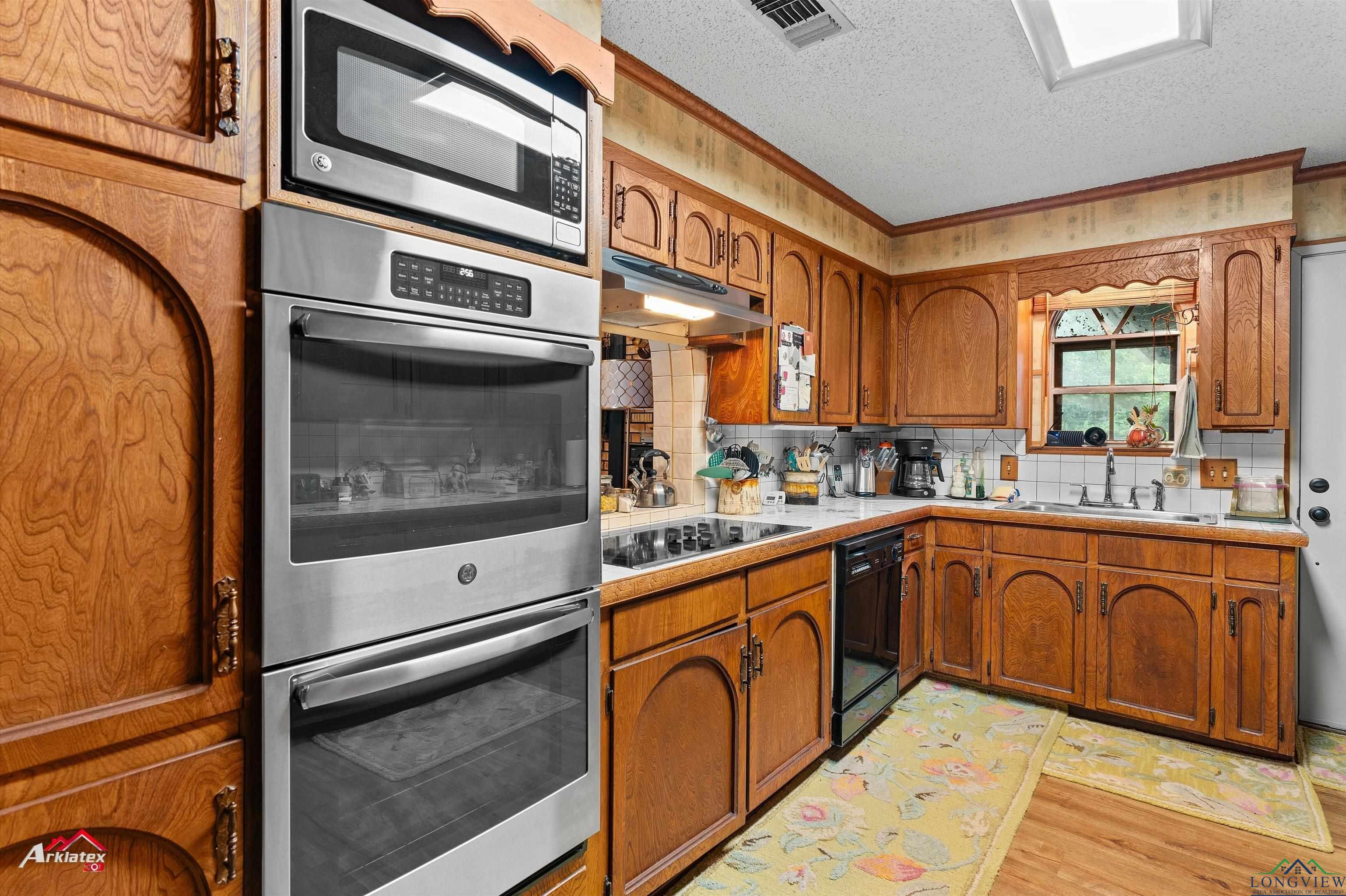 Image 1: Kitchen featuring black appliances, under cabinet range hood, light wood-type flooring, brown cabinetry, and a textured ceiling, Kitchen
