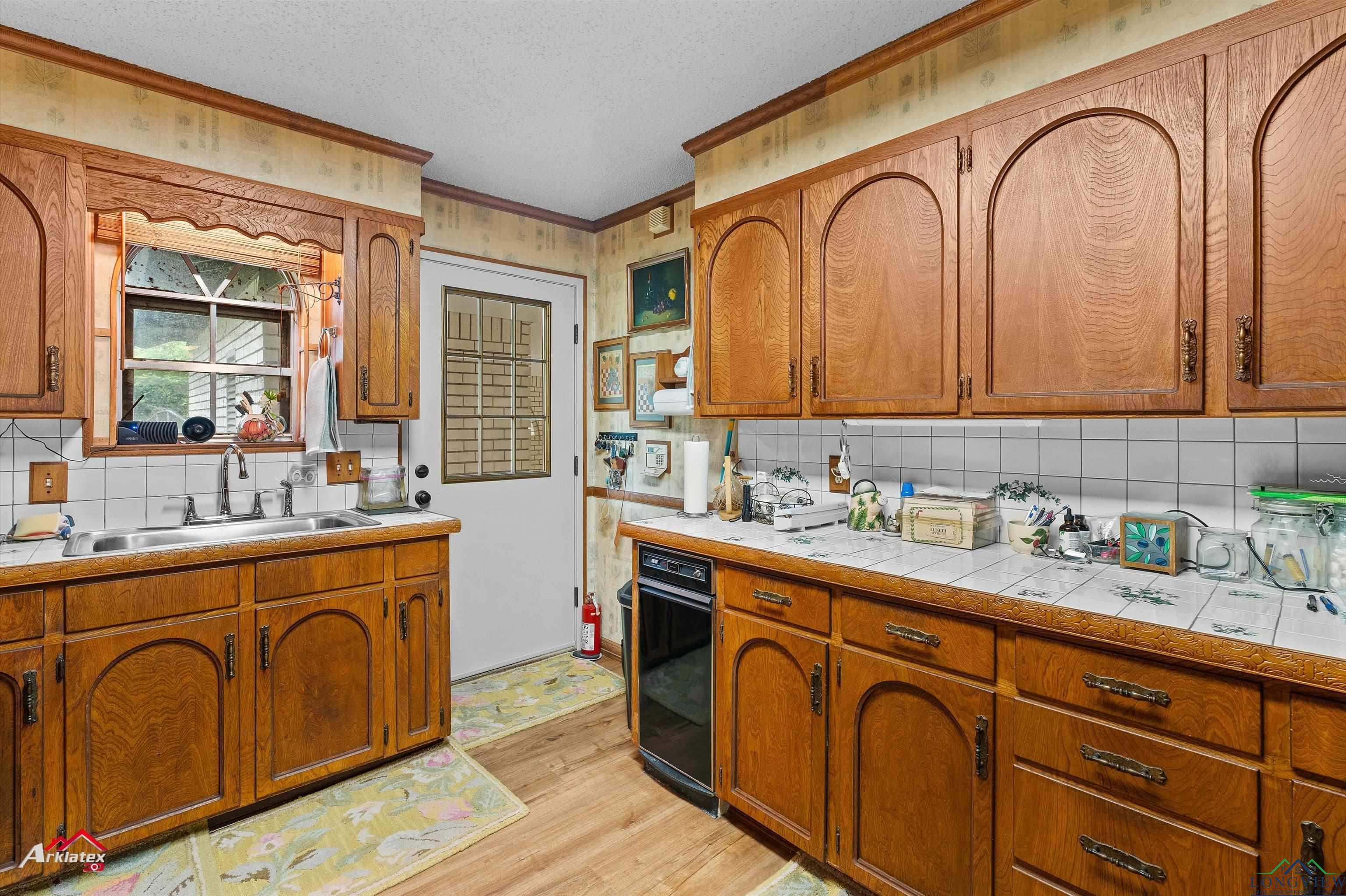 Image 2: Kitchen with backsplash, ornamental molding, brown cabinetry, light wood finished floors, and a textured ceiling, Kitchen