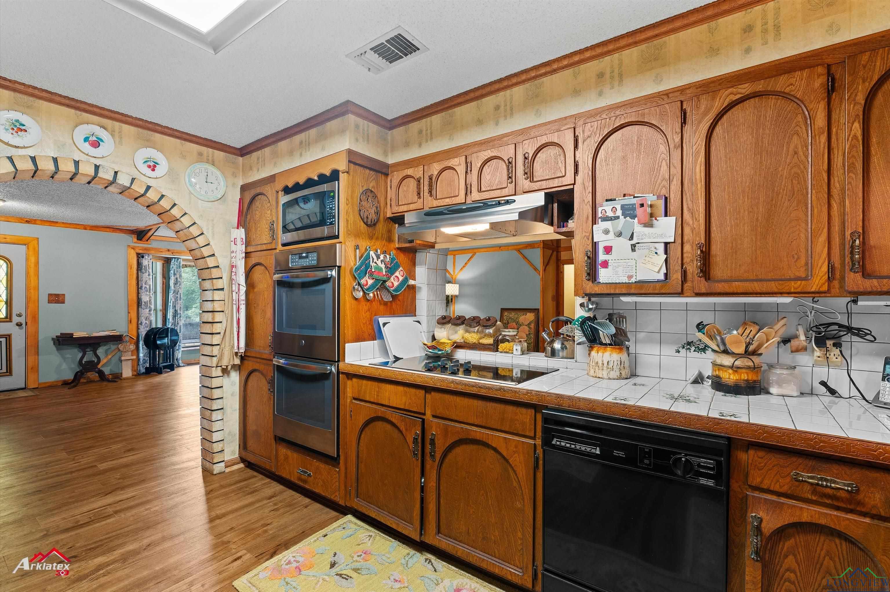 Image 3: Kitchen with black appliances, ornamental molding, tile counters, light wood finished floors, and under cabinet range hood, Kitchen