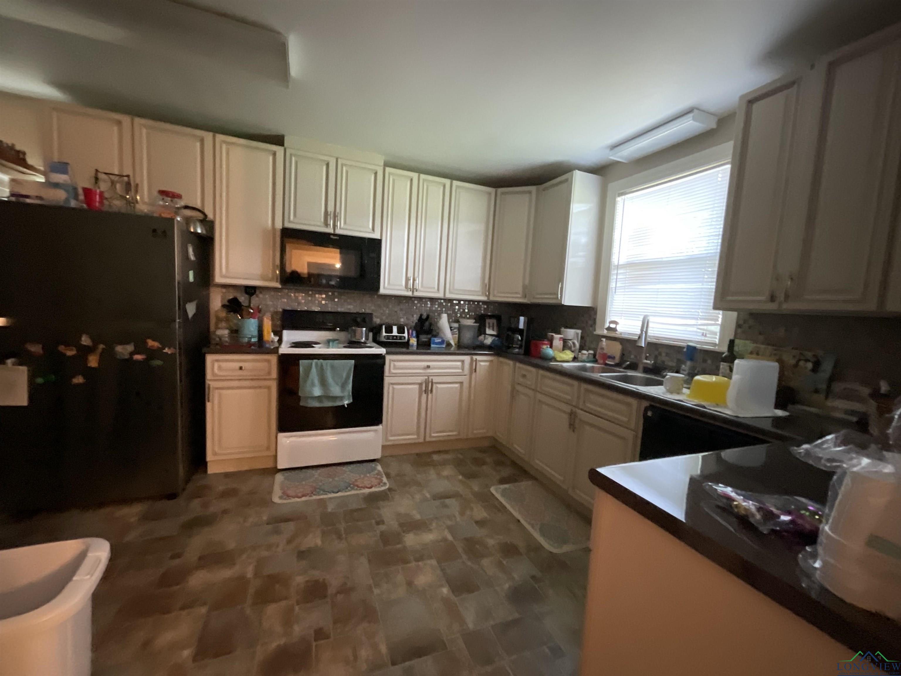 Image 3: Kitchen featuring electric range, freestanding refrigerator, black microwave, backsplash, and stone finish flooring, Kitchen