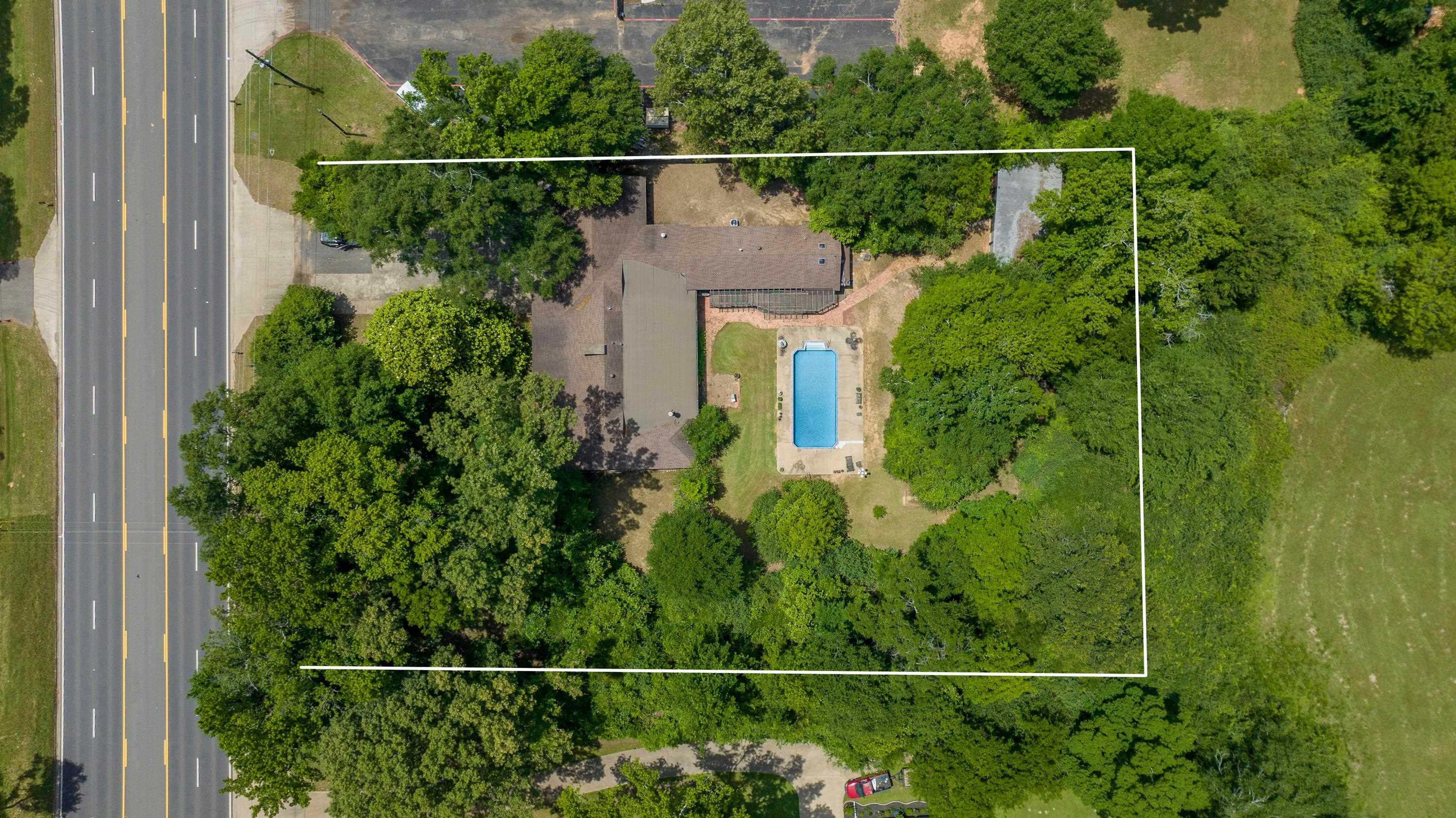 Image 2: Expansive lot featuring a main residence with an attached garage, a rectangular in-ground pool, and extensive mature trees, Aerial View