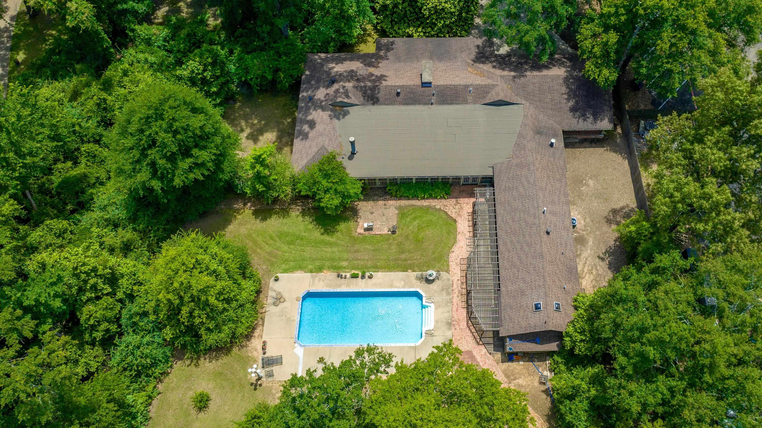 Image 3: Expansive property featuring a large residence, rectangular swimming pool with surrounding deck, and extensive mature trees, Aerial View