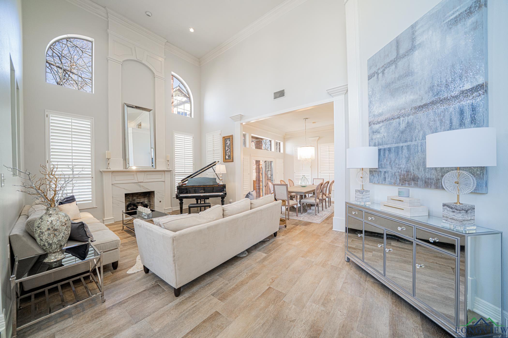 Image 3: Living area with a high ceiling, ornamental molding, plenty of natural light, light wood-style floors, and a high end fireplace, Living Room