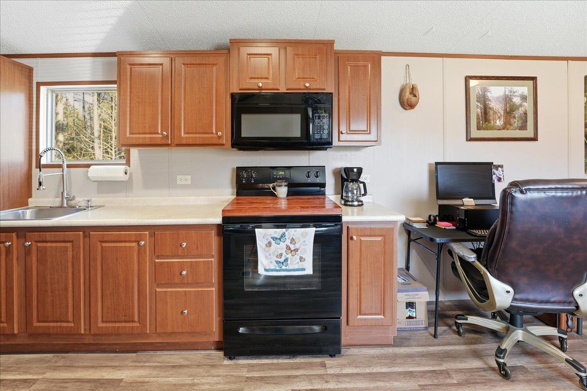 Image 3: Kitchen featuring black appliances, light countertops, a textured ceiling, light wood-style floors, and brown cabinetry, Kitchen