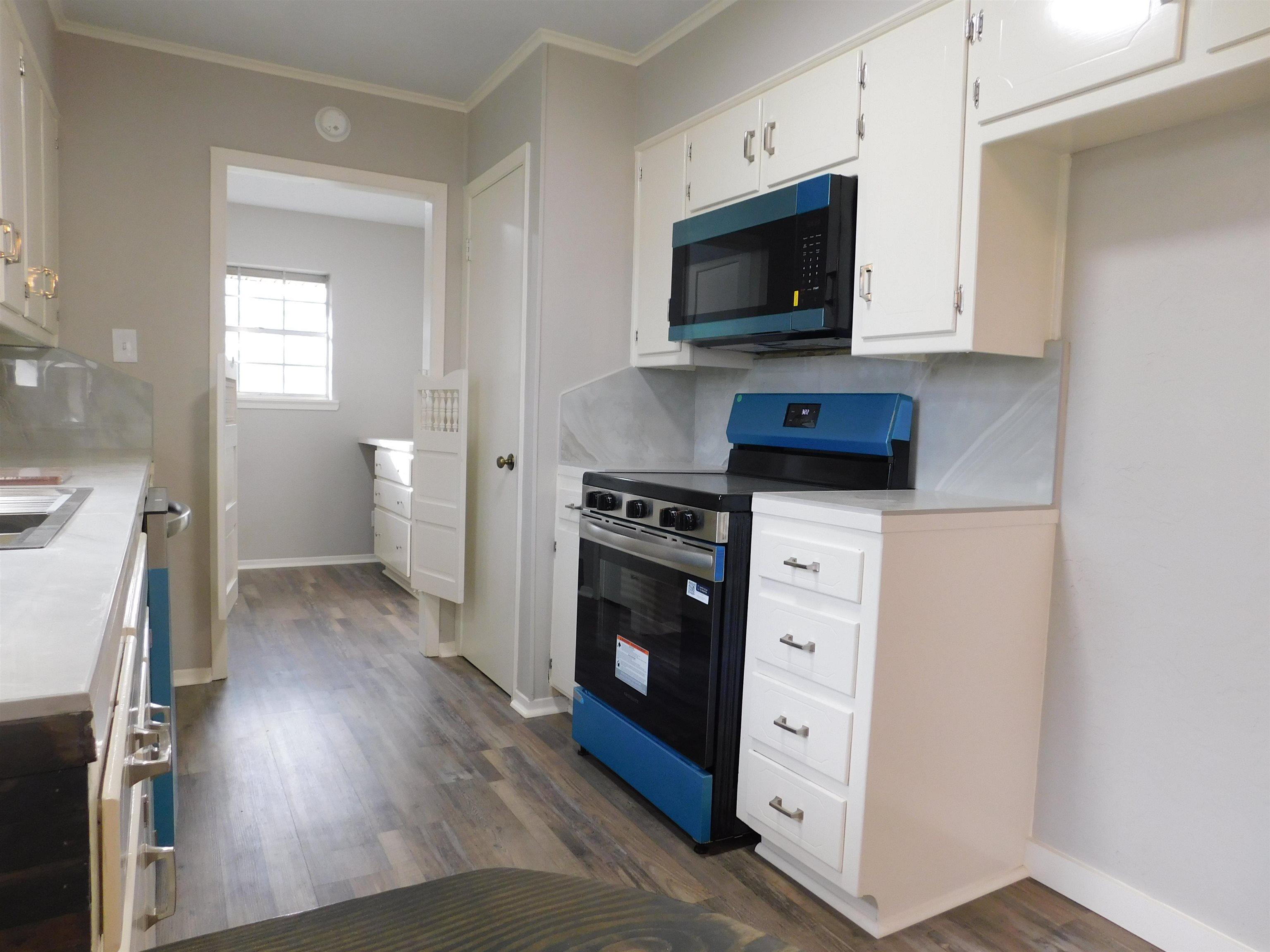 Image 2: Kitchen with electric range, light countertops, white cabinets, dark wood-style flooring, and ornamental molding, Kitchen