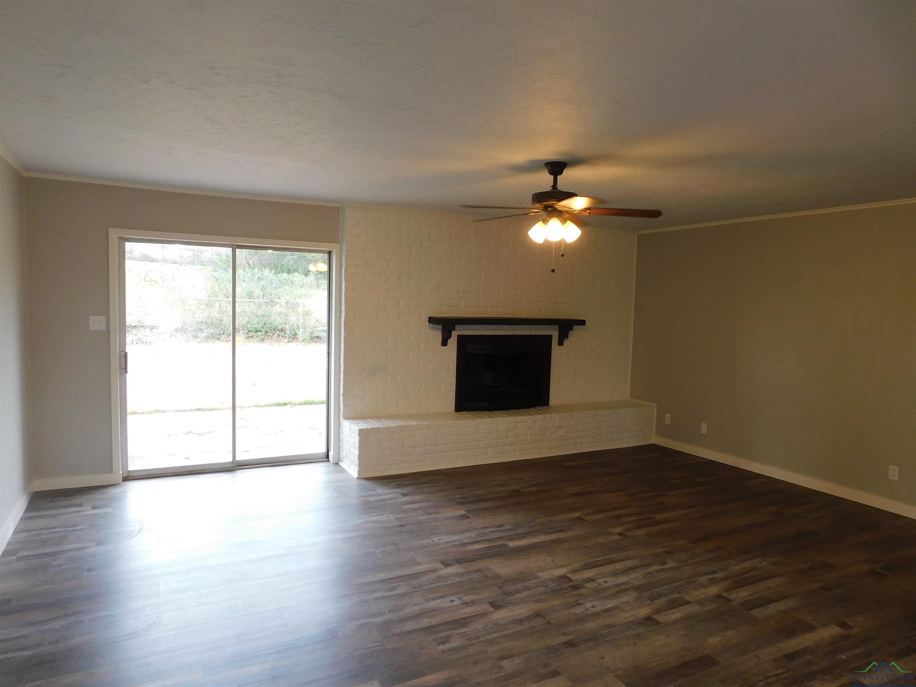 Image 3: Unfurnished living room featuring crown molding, a brick fireplace, dark wood-style floors, and ceiling fan, Living Room