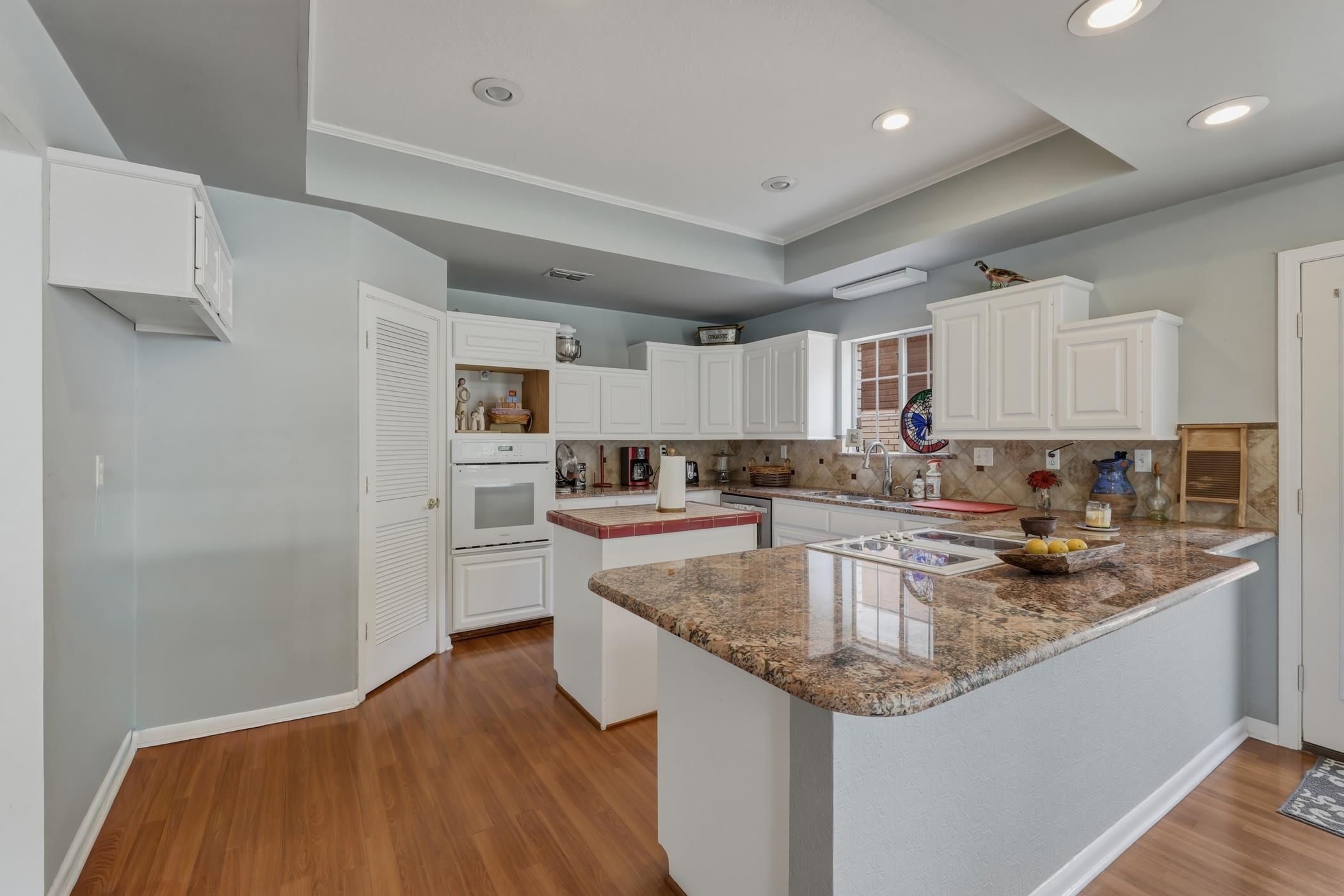 Image 3: Kitchen with a center island, a raised ceiling, white cabinets, dark wood-style flooring, and a peninsula, Kitchen