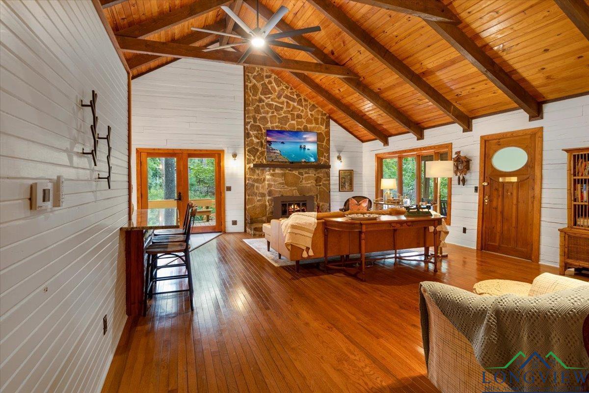 Image 2: Living area featuring wooden walls, a stone fireplace, hardwood / wood-style floors, high vaulted ceiling, and french doors, Living Room