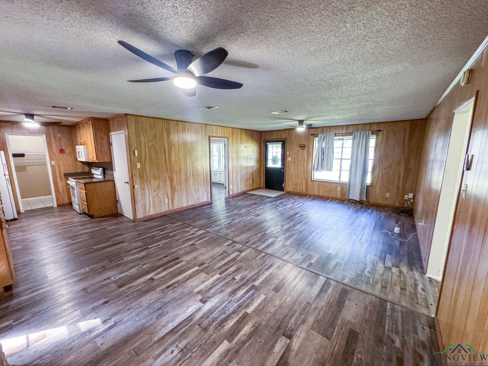 Image 3: Unfurnished living room featuring dark wood finished floors, wooden walls, a textured ceiling, and ceiling fan, Living Room