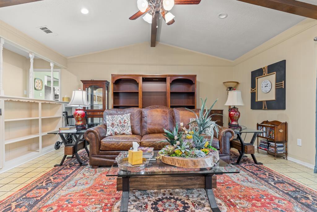 Image 1: Living area with a ceiling fan, beam ceiling, and light tile patterned floors, Living Room