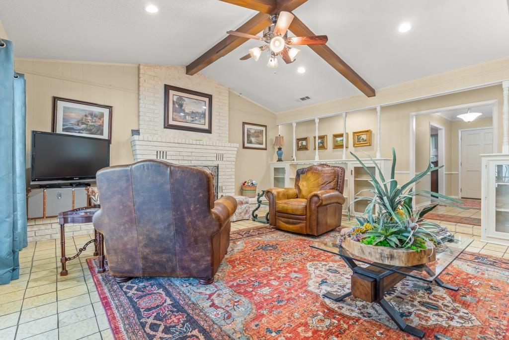 Image 3: Living area with light tile patterned flooring, a brick fireplace, beamed ceiling, a ceiling fan, and recessed lighting, Living Room
