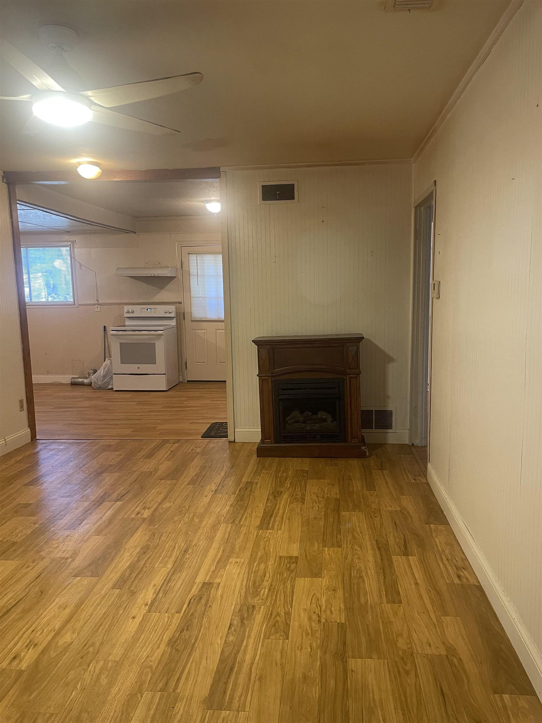 Image 3: Living area featuring wood-finish flooring, a ceiling fan with integrated lighting, and a decorative fireplace, Living Room